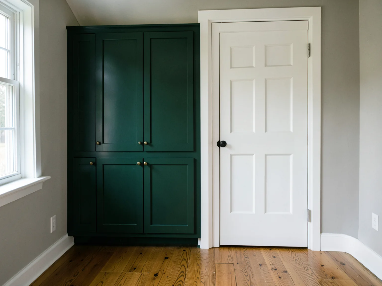 Forest-green shaker cabinets beside a white six-panel door with crisp painted trim (illustrative, generated).